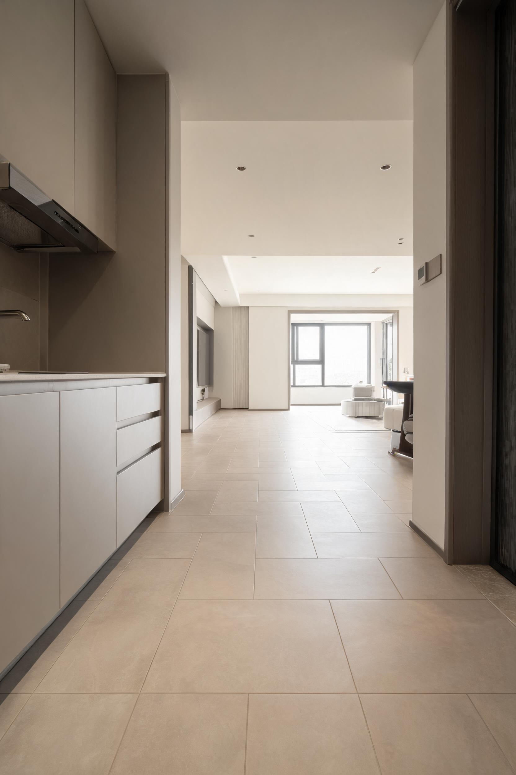 Large-format porcelain tile running from kitchen through into the adjacent living space with no transition strip -- the continuous floor eliminates every visual boundary between the two rooms.