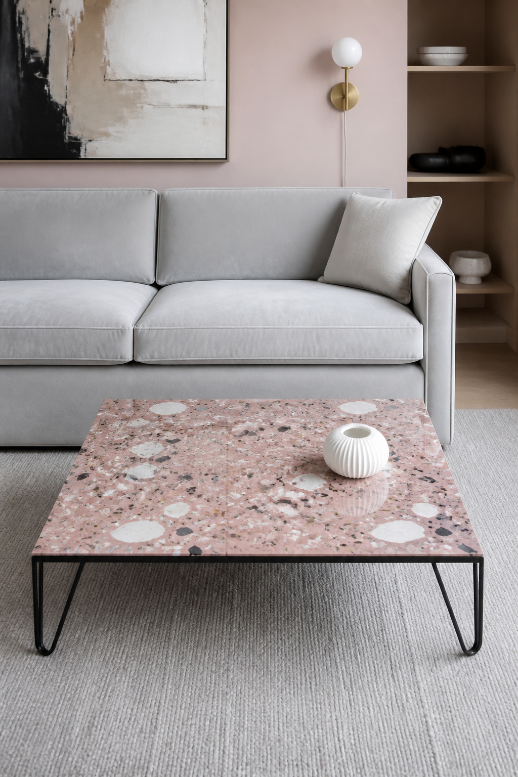 A terrazzo coffee table in a dusty rose epoxy matrix with marble, obsidian, and brass-chip aggregate reads as a floor-level art object in a contemporary living room, the chip pattern unique and irrepeatable.