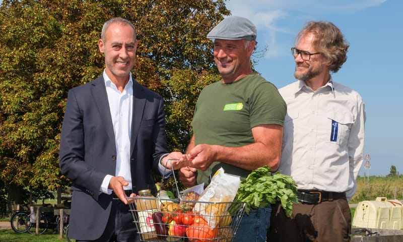 Boer Martin overhandigt een mandje lokale biodiverse producten aan wethouder Kasmi