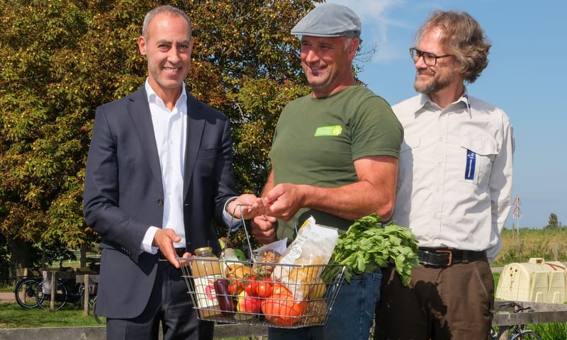 Boer Martin overhandigt een mandje lokale biodiverse producten aan wethouder Kasmi