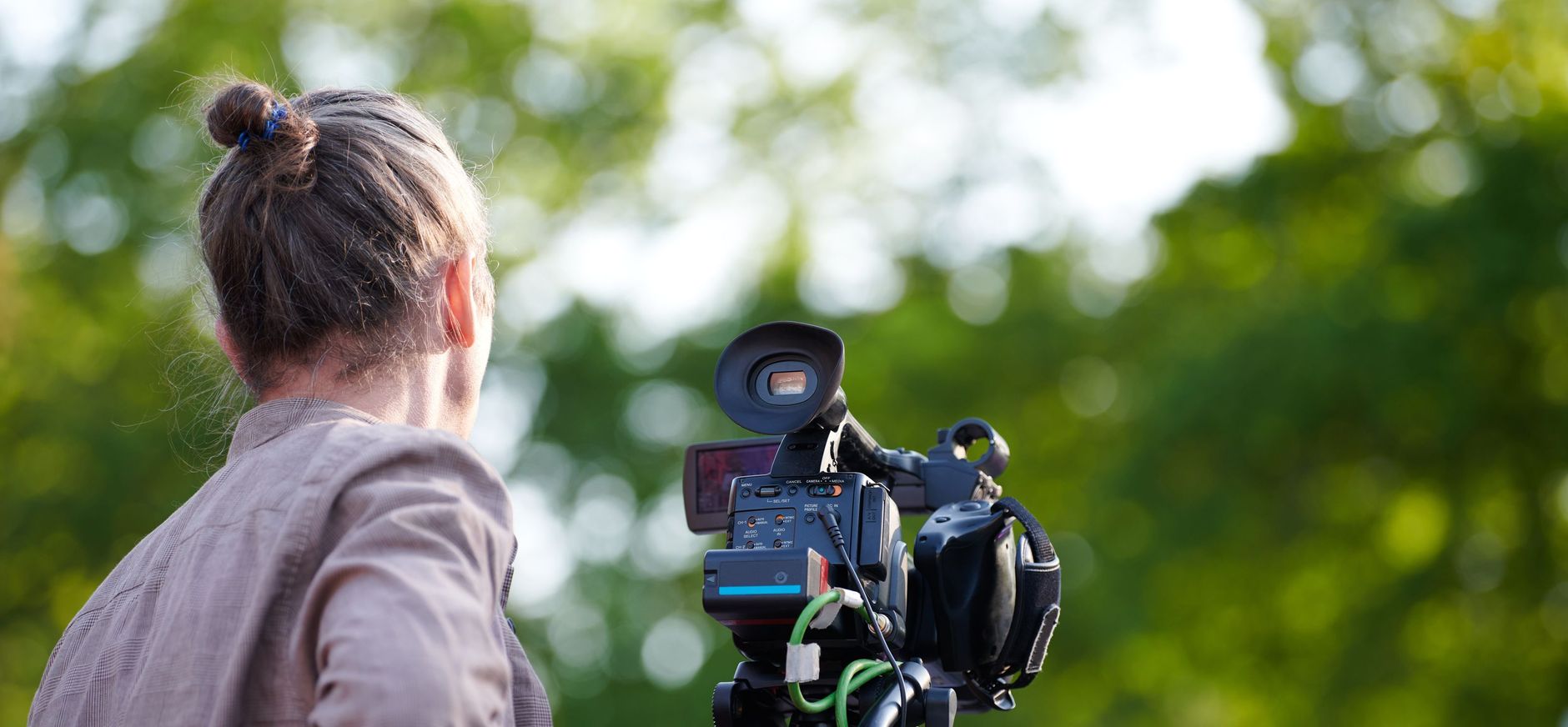 Persoon met een camera op een statief ervoor met uitzicht op groene achtergrond