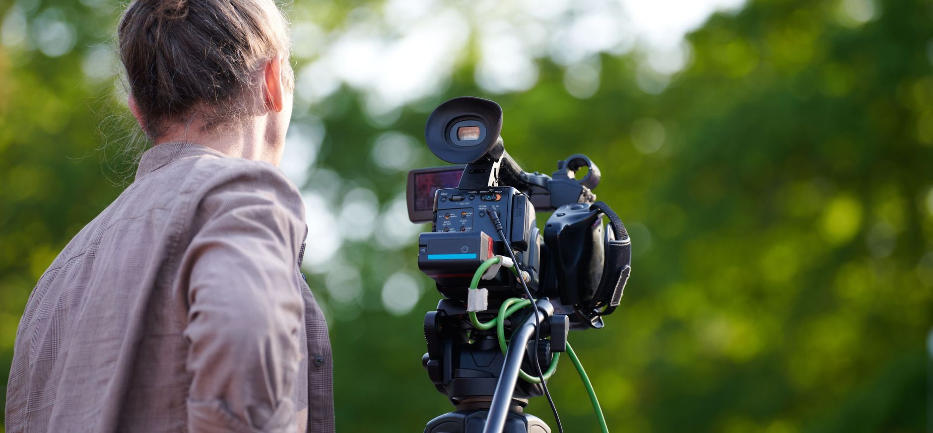 Persoon met een camera op een statief ervoor met uitzicht op groene achtergrond