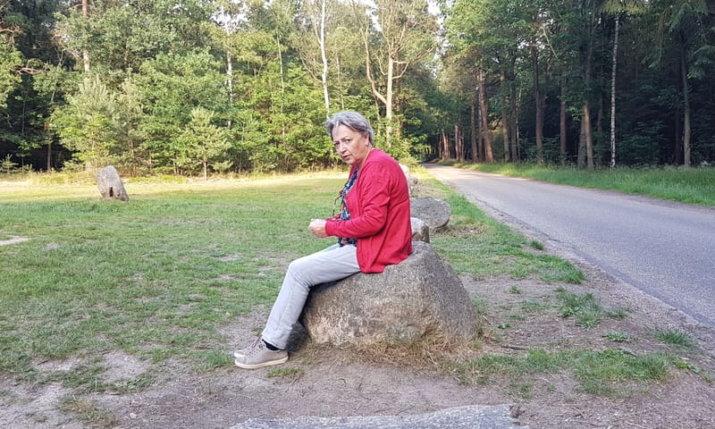 Els Boon van LC Fryslân zit op een steen op een open veld in een bos.