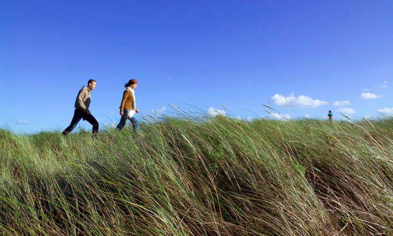 twee wandelaars in de duinen met op de achtergrond een rode vuurtoren