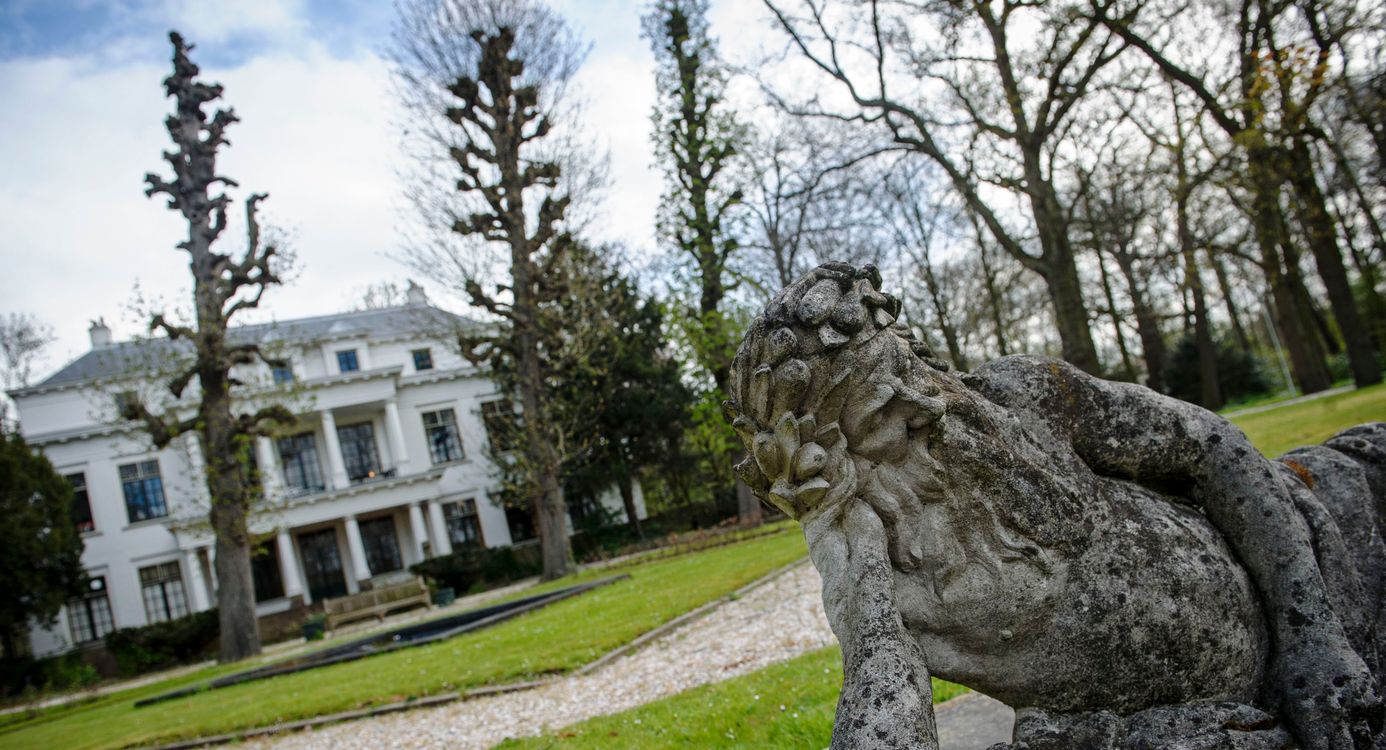 Op de voorgrond een oud standbeeld, op de achtergrond het witte hoofdgebouw van landgoed De Tempel