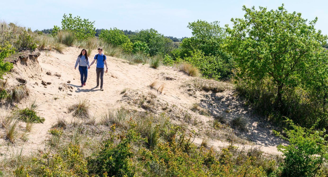 Twee wandelaars die door de duinen lopen