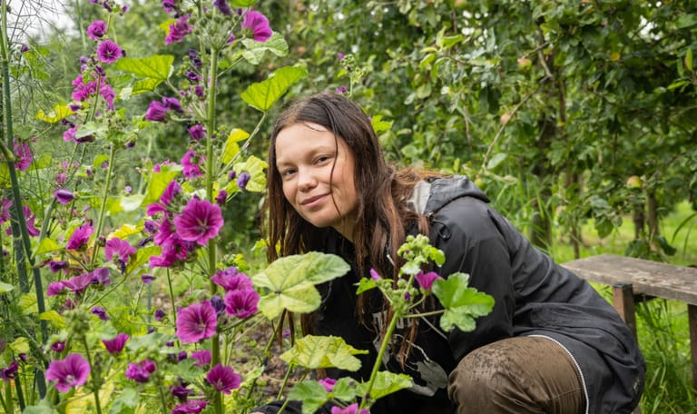 Dame (Ida Simonsen) die tussen de bloemen door naar de camera kijkt