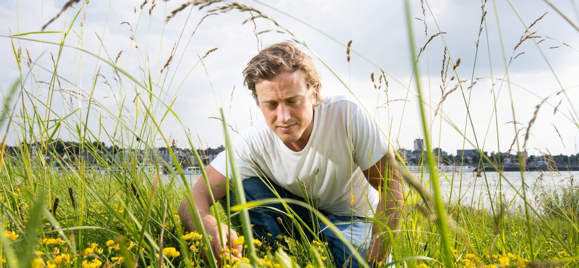 Een man die op zijn hurken in het groen zit om de plantjes te bestuderen