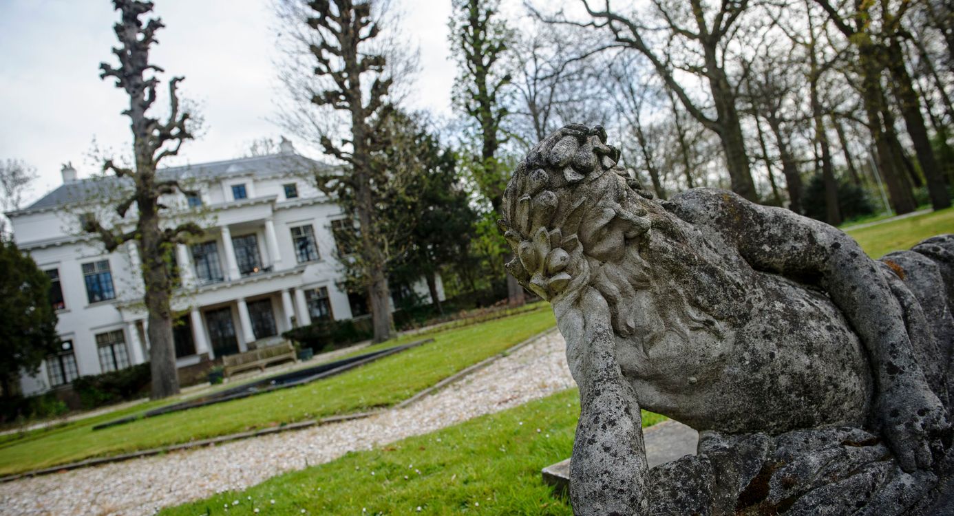 Op de voorgrond een oud standbeeld, op de achtergrond het witte hoofdgebouw van landgoed De Tempel