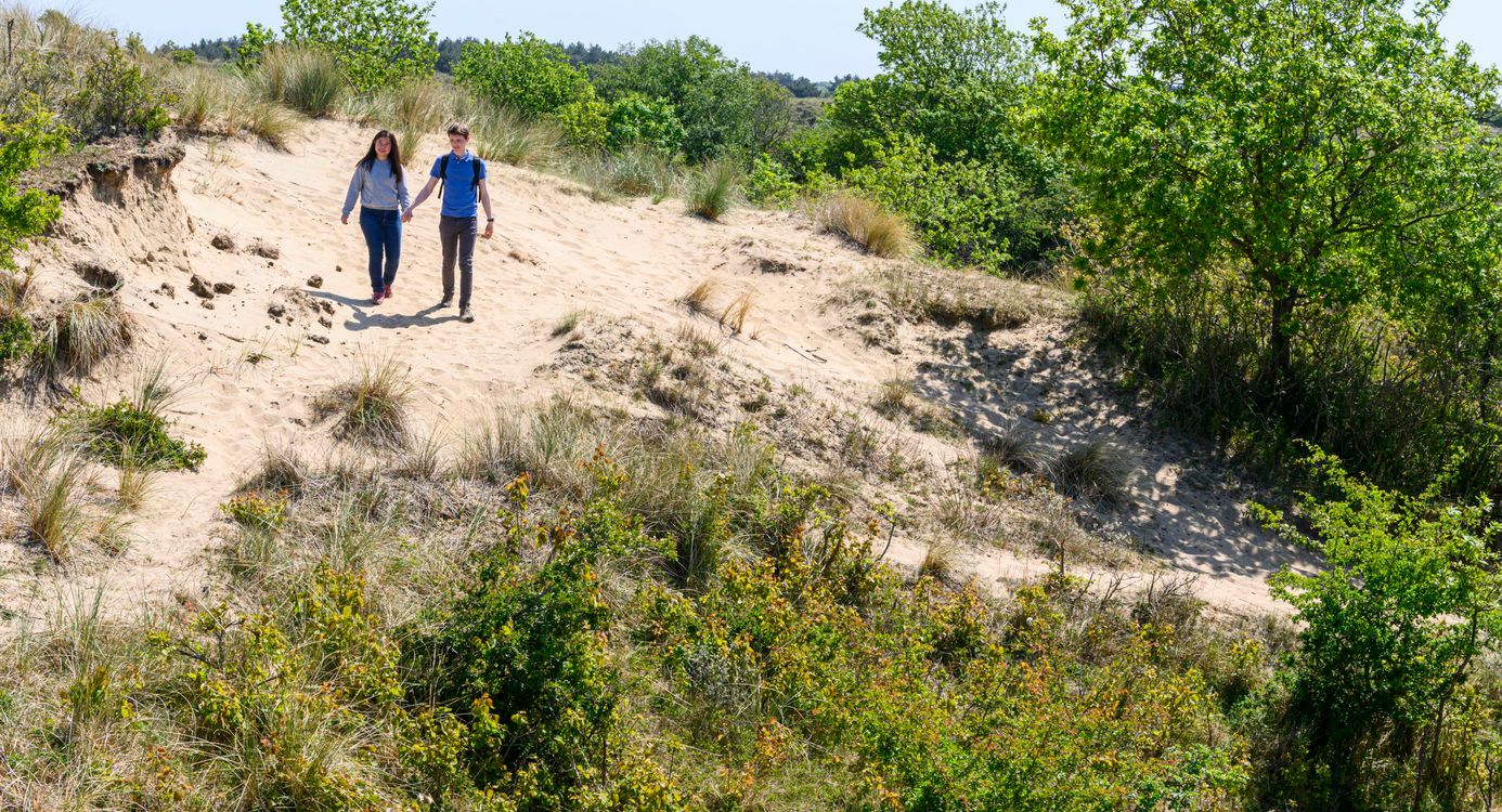 Twee wandelaars die door de duinen lopen