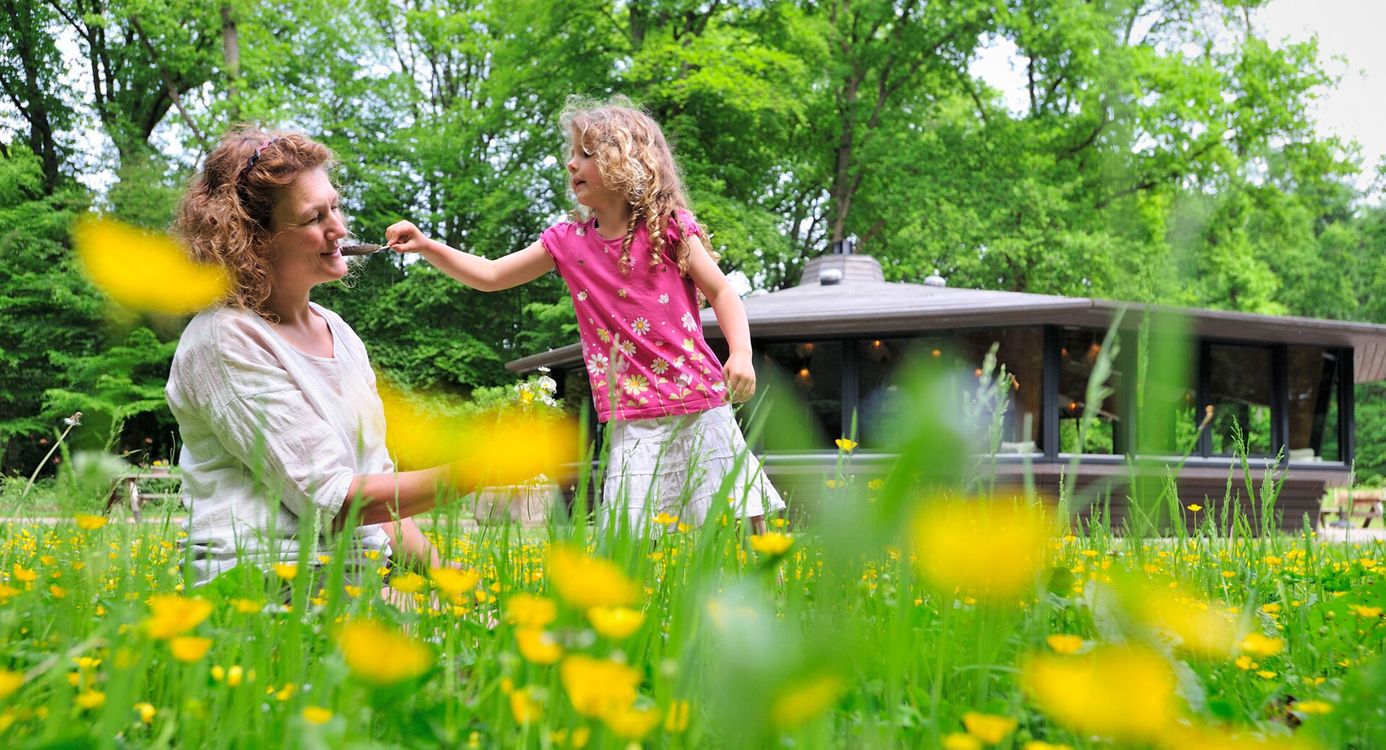 Vrouw en meisje tussen de gele bloemen, meisje kietelt de vrouw met een veer
