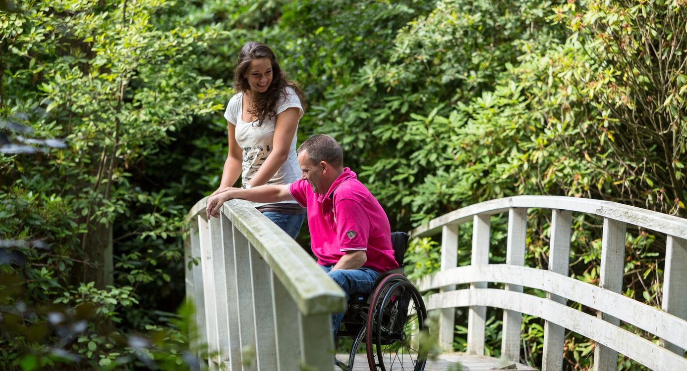 Man in een rolstoel en een dame, samen op een wit bruggetje