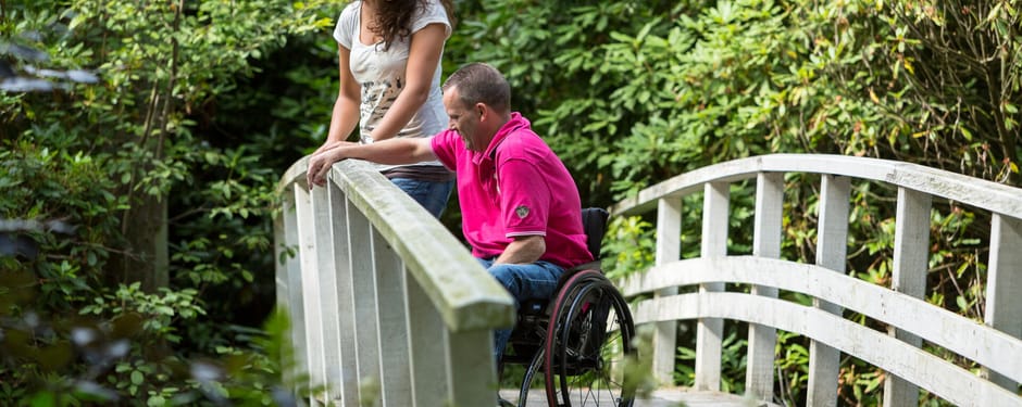 Man in een rolstoel en een dame, samen op een wit bruggetje