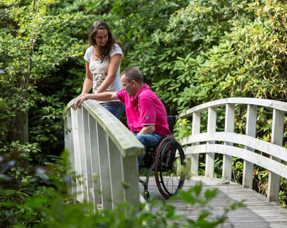Man in een rolstoel en een dame, samen op een wit bruggetje