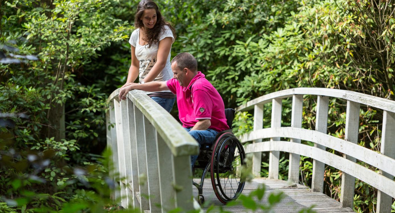 Man in een rolstoel en een dame, samen op een wit bruggetje
