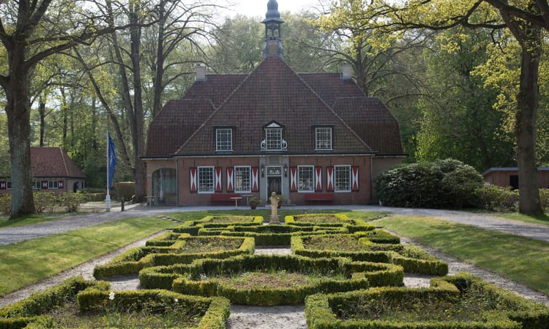 Vooraanzicht van het hoofdgebouw van landgoed De Slotplaats met ervoor een patroon van buxushaagjes