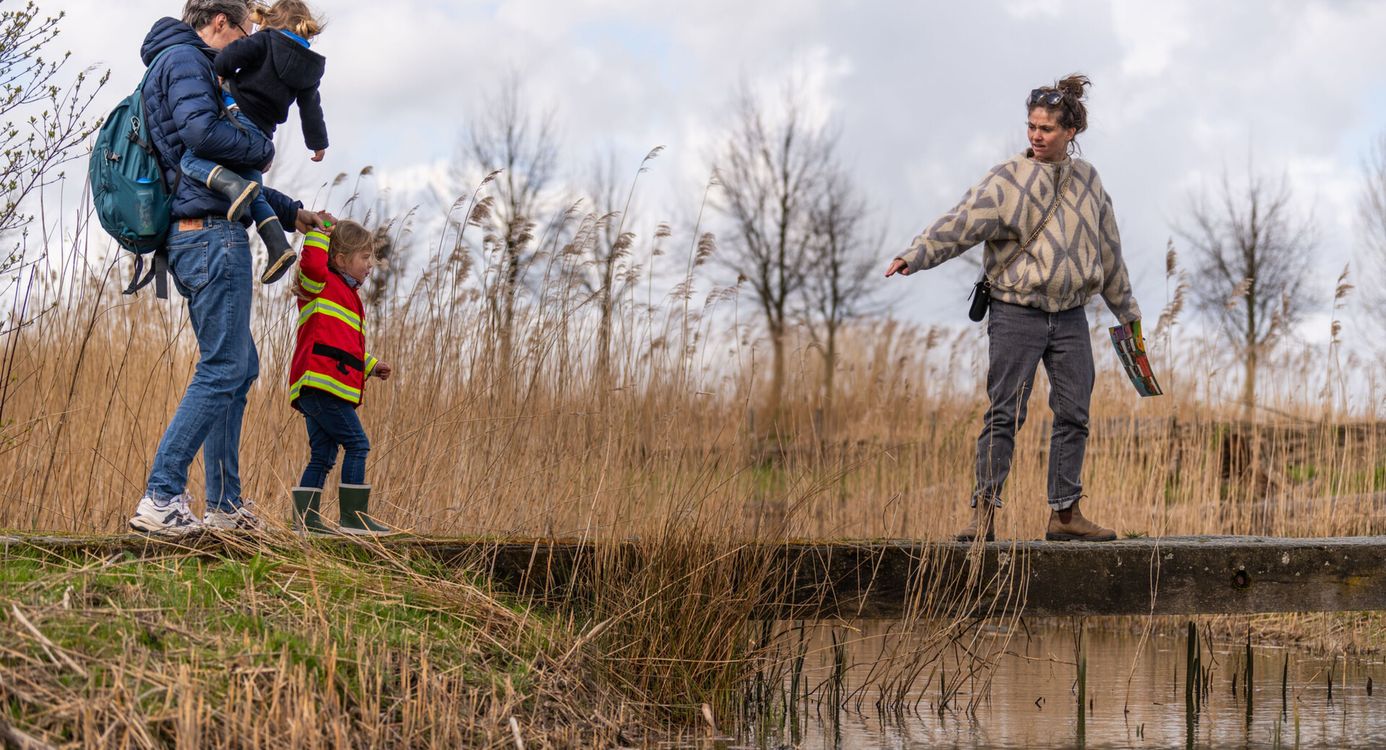 Twee volwassenen die met twee kinderen over een bruggetje lopen, met riet er omheen