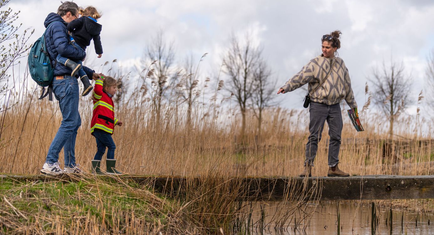Twee volwassenen die met twee kinderen over een bruggetje lopen, met riet er omheen