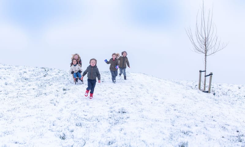 Kinderen rennen van een besneeuwde heuvel naar beneden