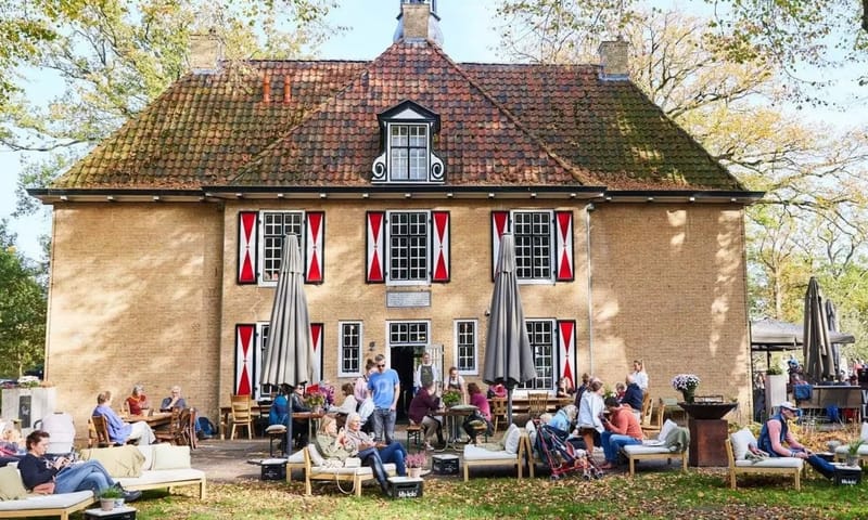 Gebouw met rood-witte luiken met daarvoor mensen op een terras