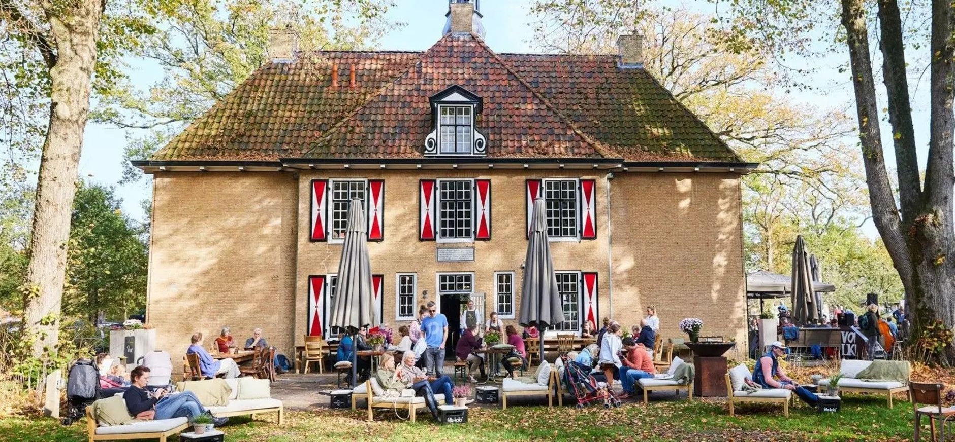 Gebouw met rood-witte luiken met daarvoor mensen op een terras
