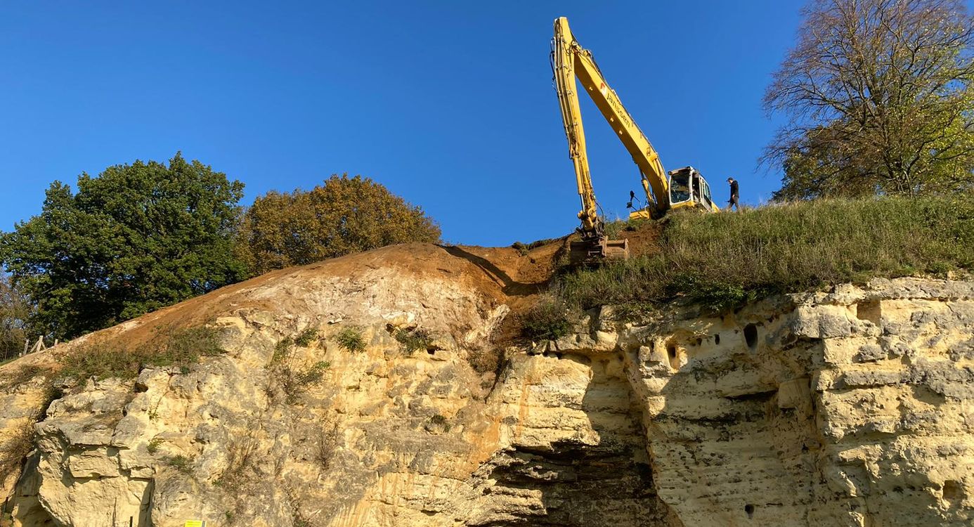 Een graafmachine schraapt begroeiing van een kalkrots in het Geuldal