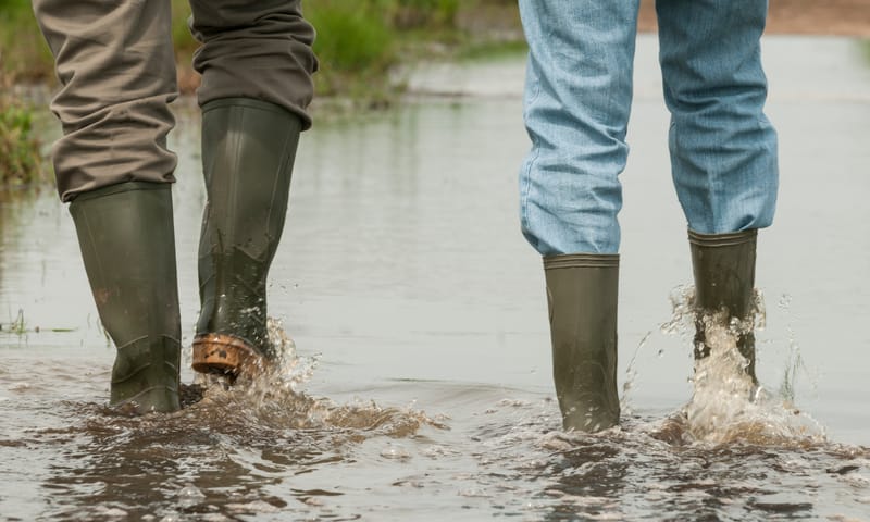 twee paar benen met laarzen die door het water stappen