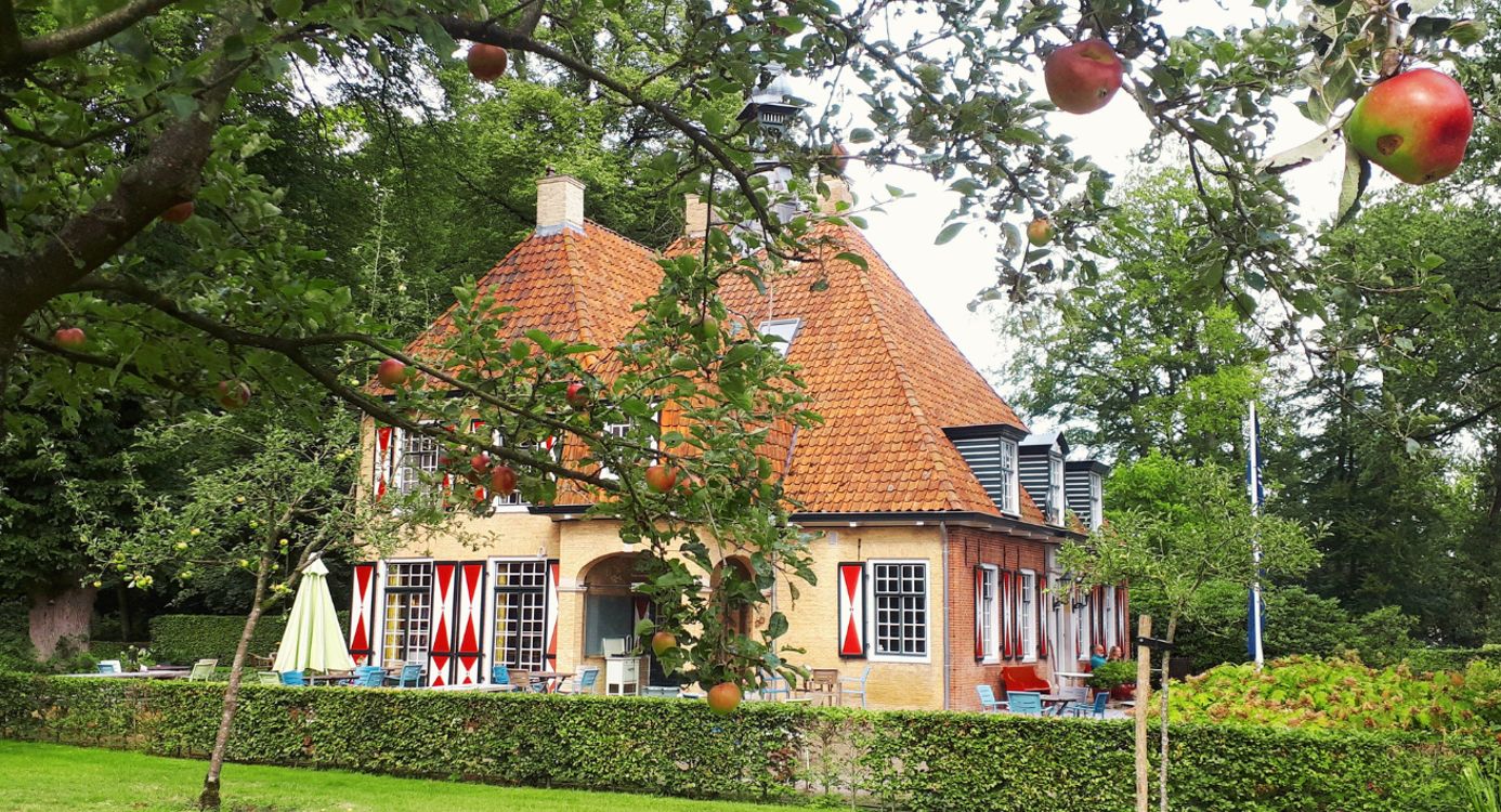 Foto van het landhuis op landgoed De Slotplaats, met op de voorgrond de vruchtdragende bomen in de boomgaard.