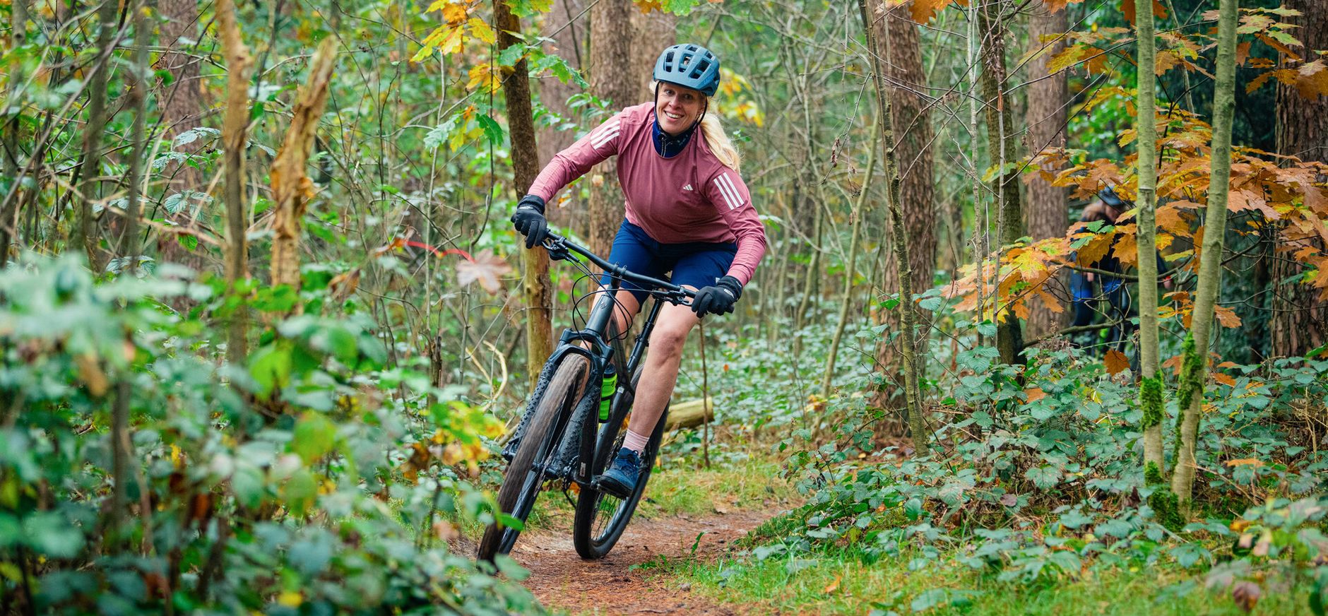 Vrouwelijke mountainbiker die door het bos op je af komt rijden