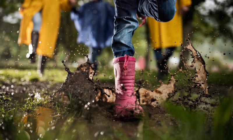 Kinderen rennen met laarzen door een regenplas