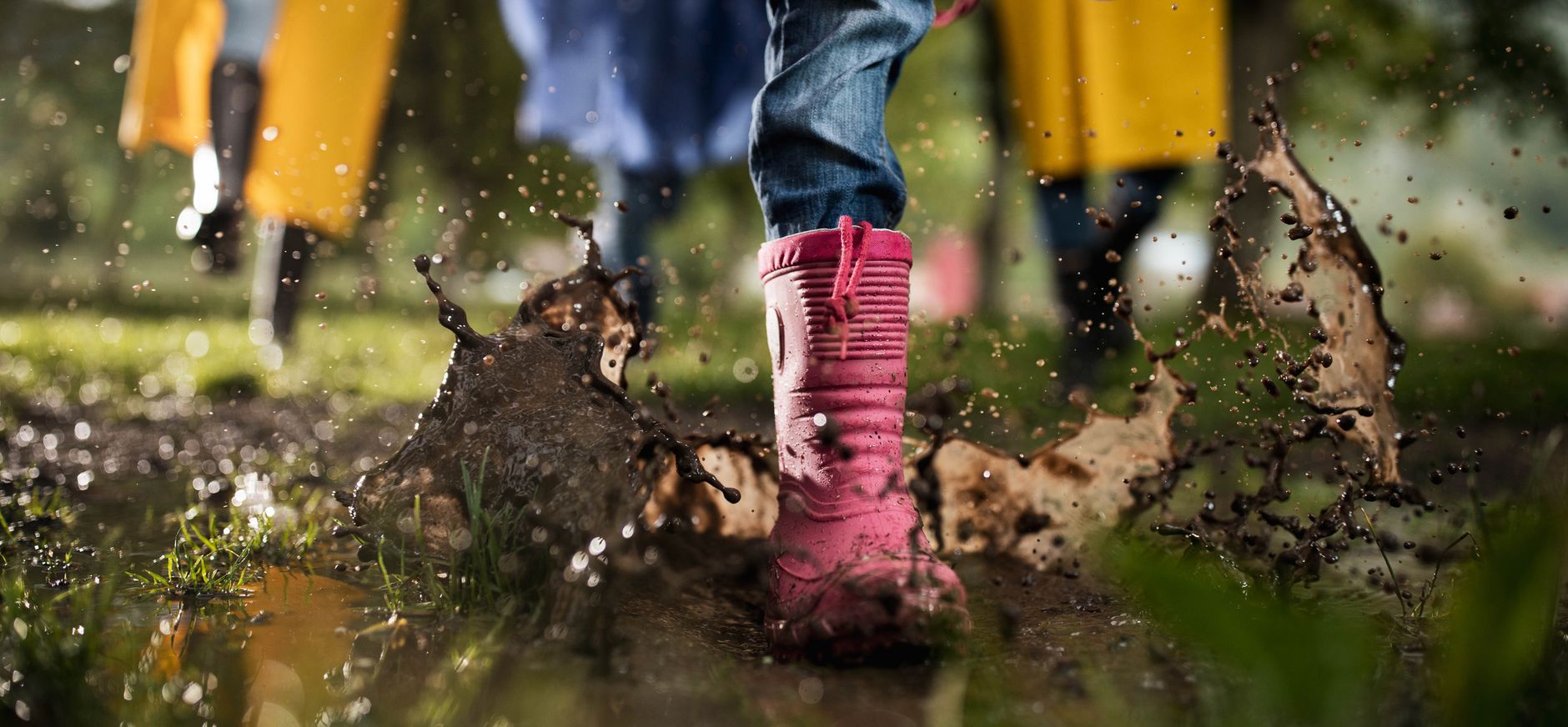 Kinderen rennen met laarzen door een regenplas