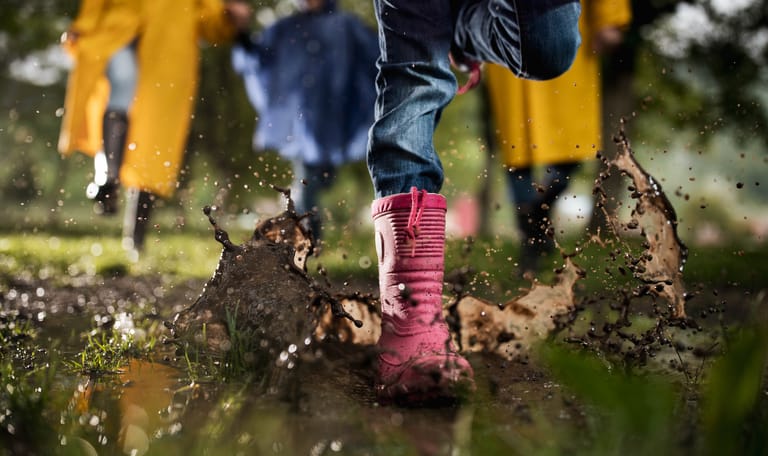 Kinderen met regenlaarzen spelen buiten na een regenbui.