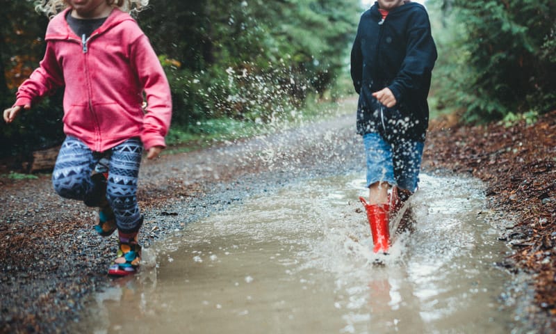 Kinderen spelen regenplastikkertje bij regenplassen.