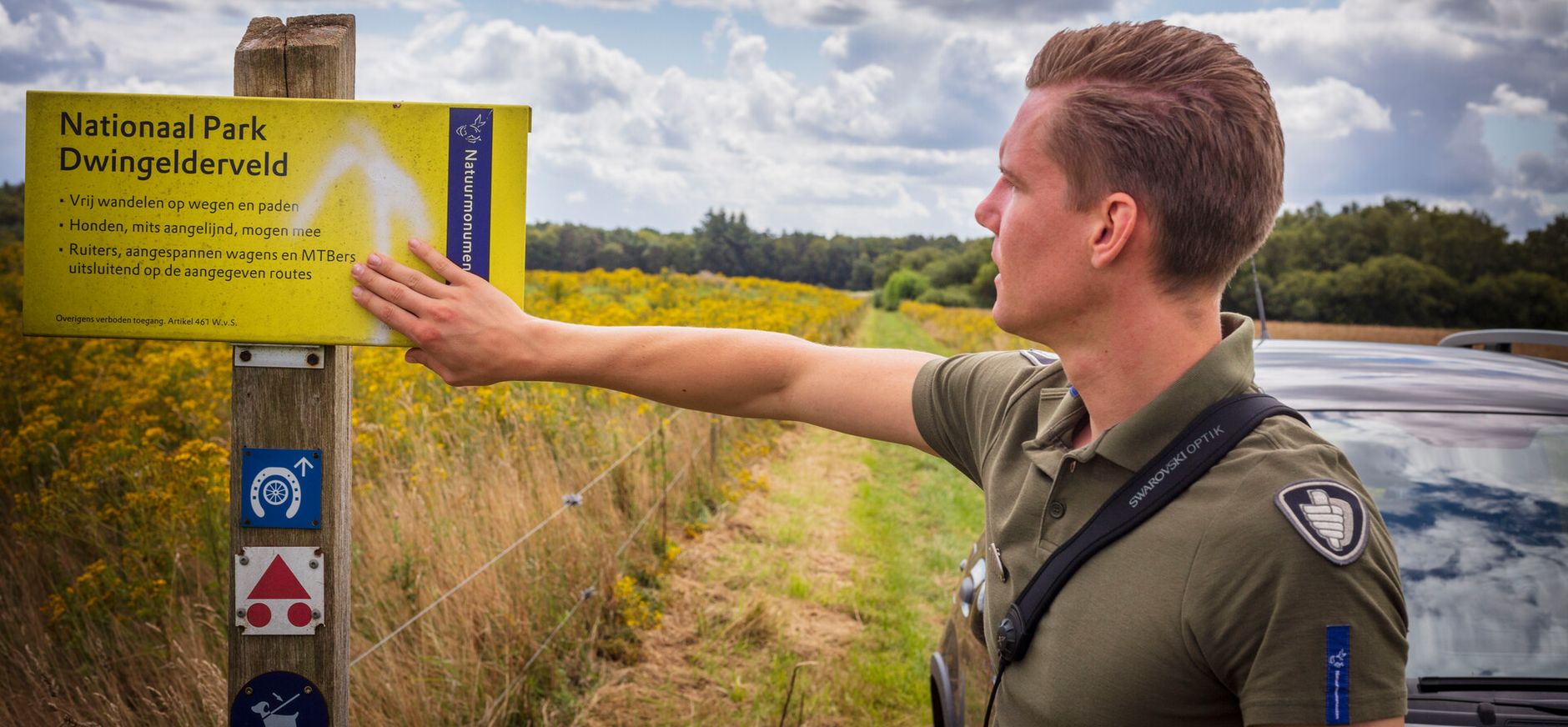 BOA kijkt weg van de camera, naar een gebiedsbord van Natuurmonumenten