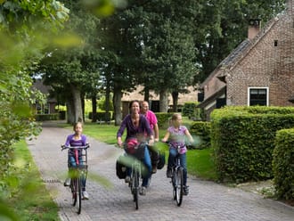 Gezin fietst door esdorp met oude boederijen en grote eikenbomen