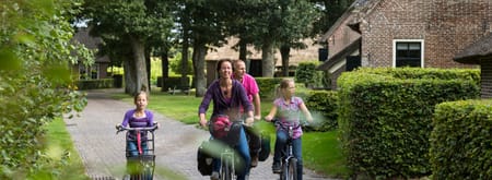 Gezin fietst door esdorp met oude boederijen en grote eikenbomen 