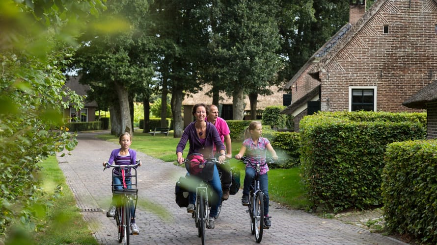 Gezin fietst door esdorp met oude boederijen en grote eikenbomen 