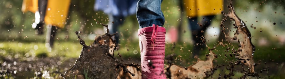 Kinderen rennen met laarzen door een regenplas