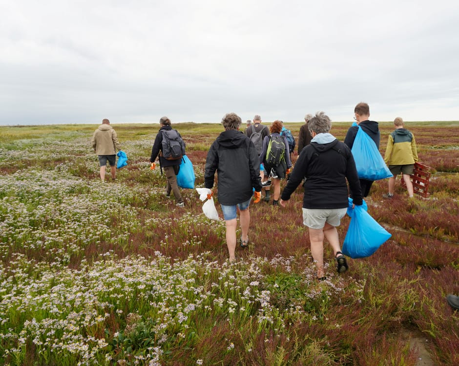 Een groep mensen loopt met vuilniszakken over Griend