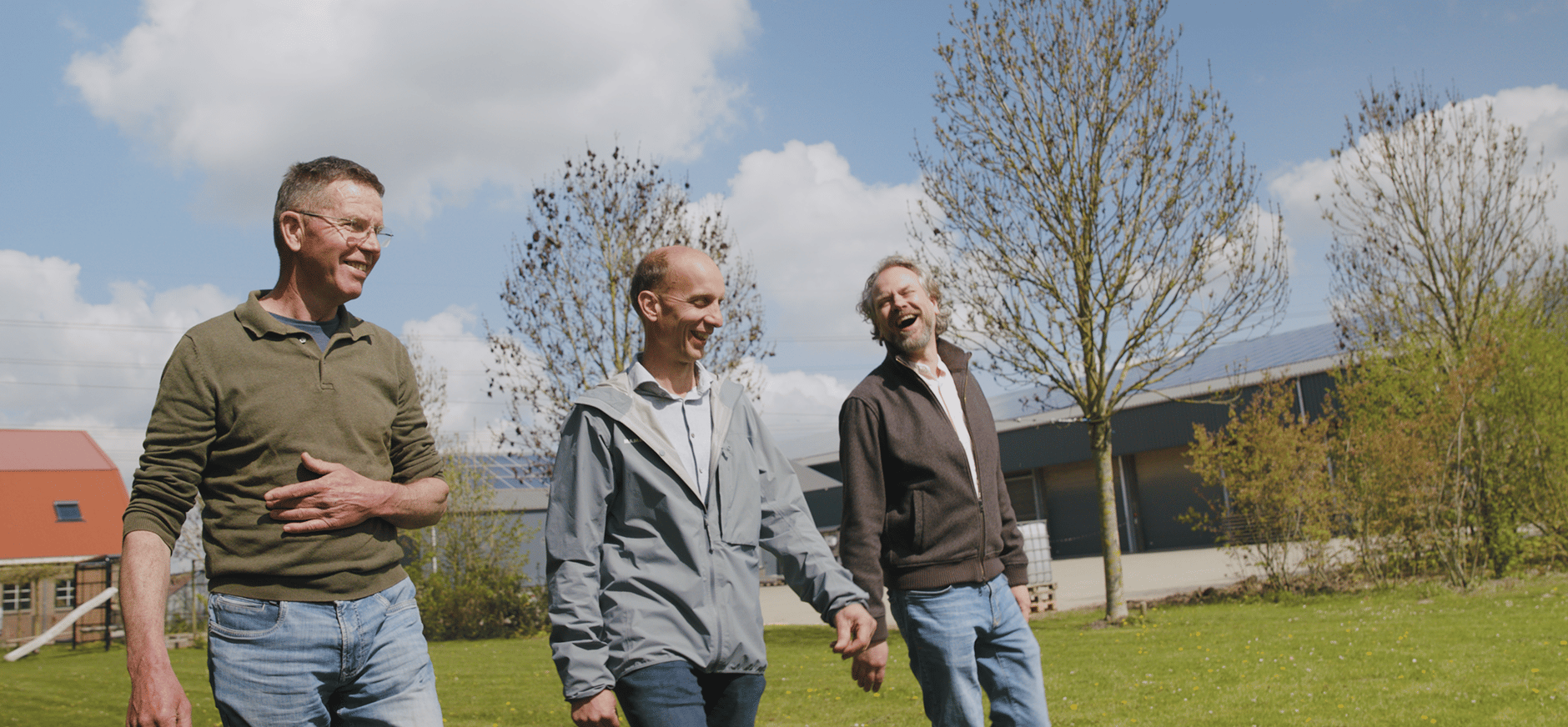 Drie mannen die over een grasveld lopen, met bomen op de achtergrond