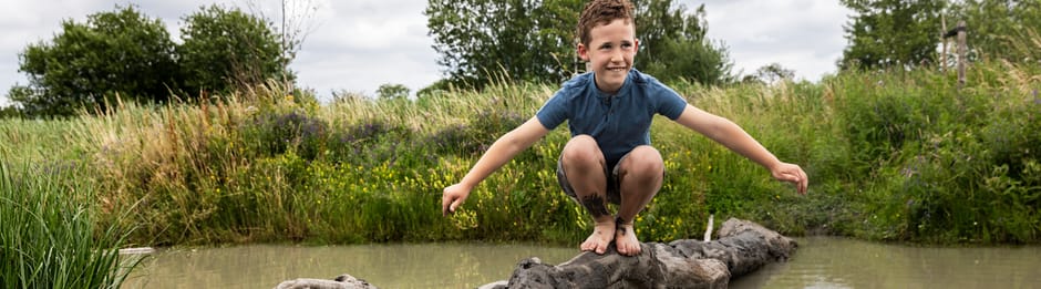 Jongen zit op boomstam in het water