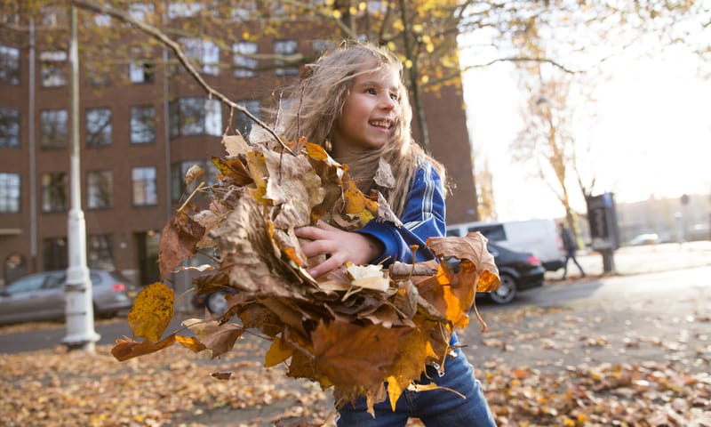 Meisje speelt met herfstbladeren in stedelijke oemgeving