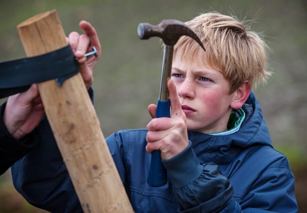 Jongen met hamer in de hand helpt met boom planten 