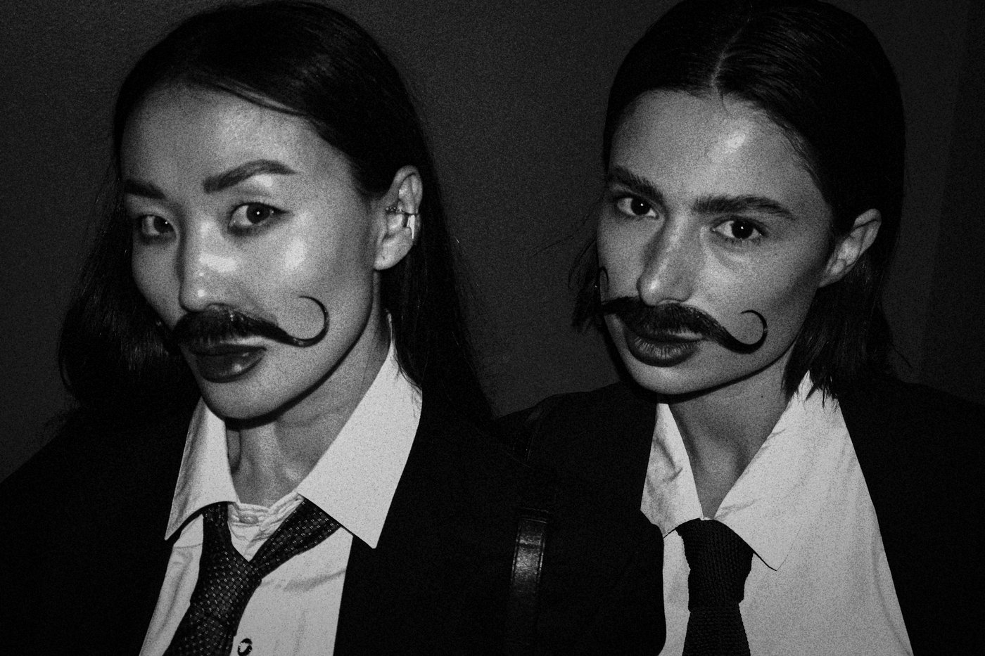 two women with fake facial hair in suits
