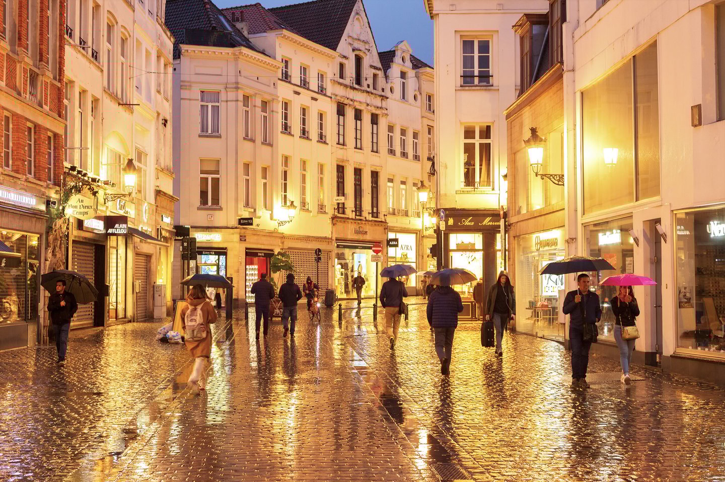 Crowd of people walking by Old Town shopping street of Brussels in the rain at dusk