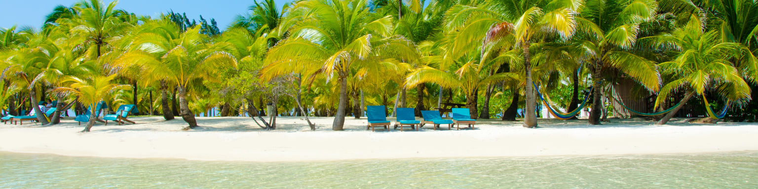 Blue loungers under palm trees on a white, sandy beach in South Water Caye, Belize