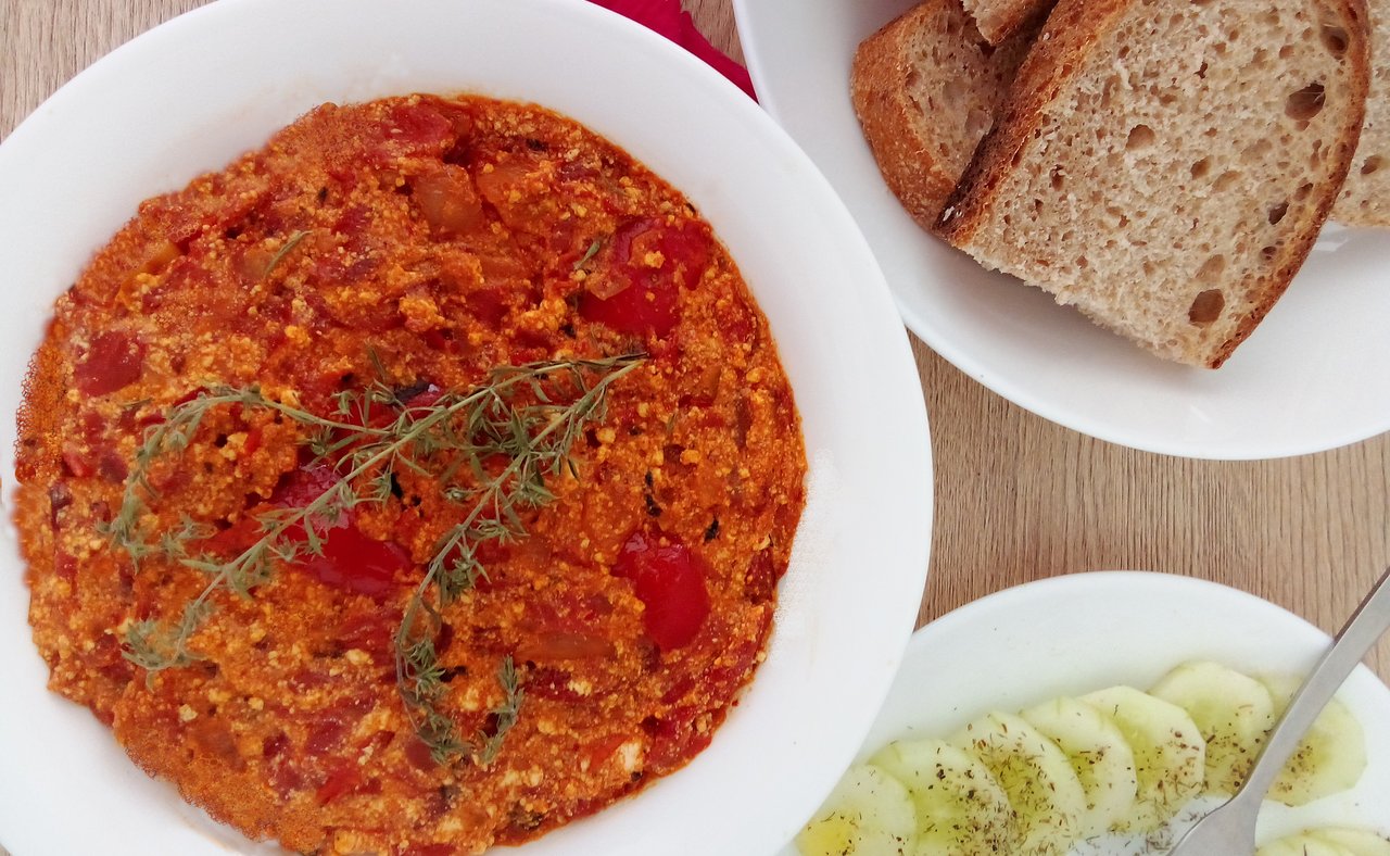 A bowl of Albanian fergese on a table with bread and a salad