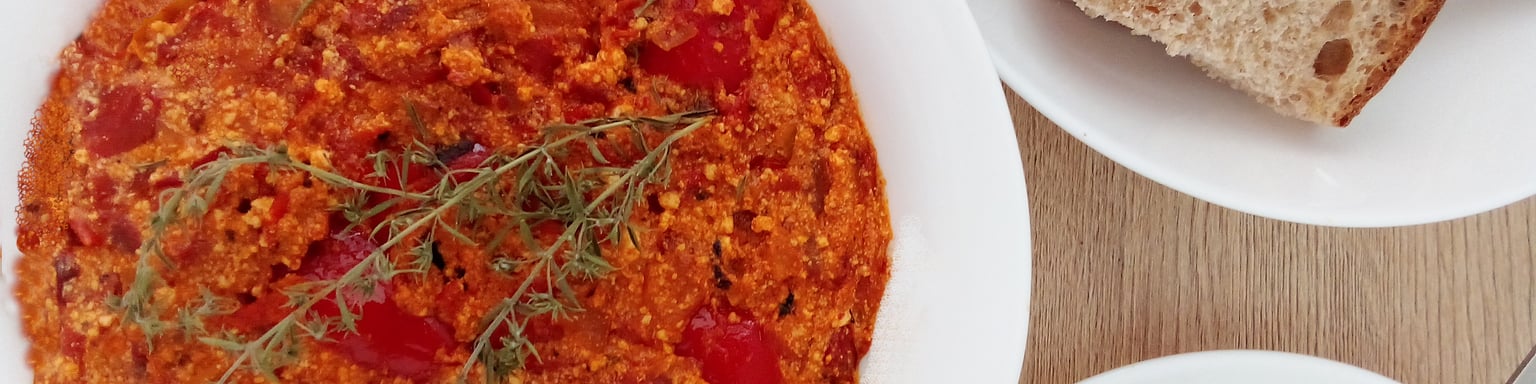 A bowl of Albanian fergese on a table with bread and a salad