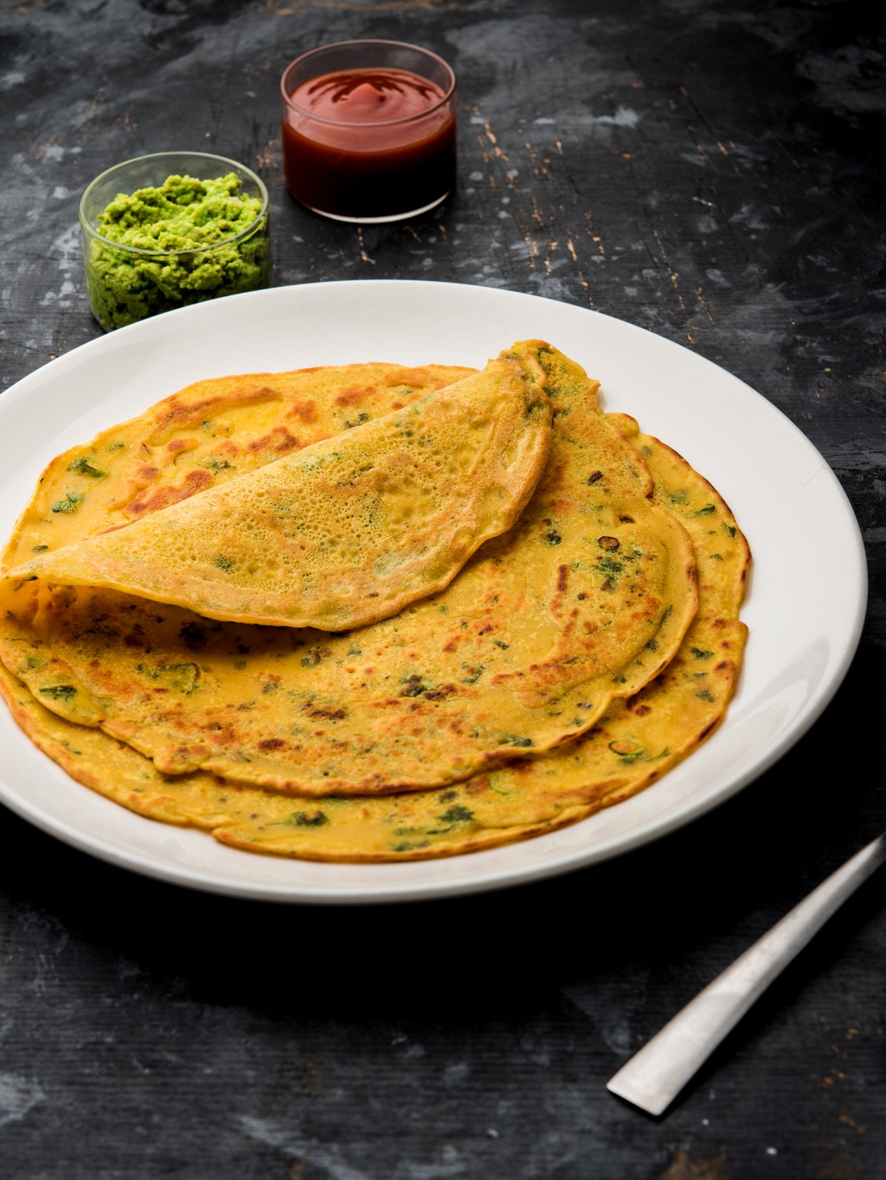 Besan chilla, a savoury pancake, served with sauces