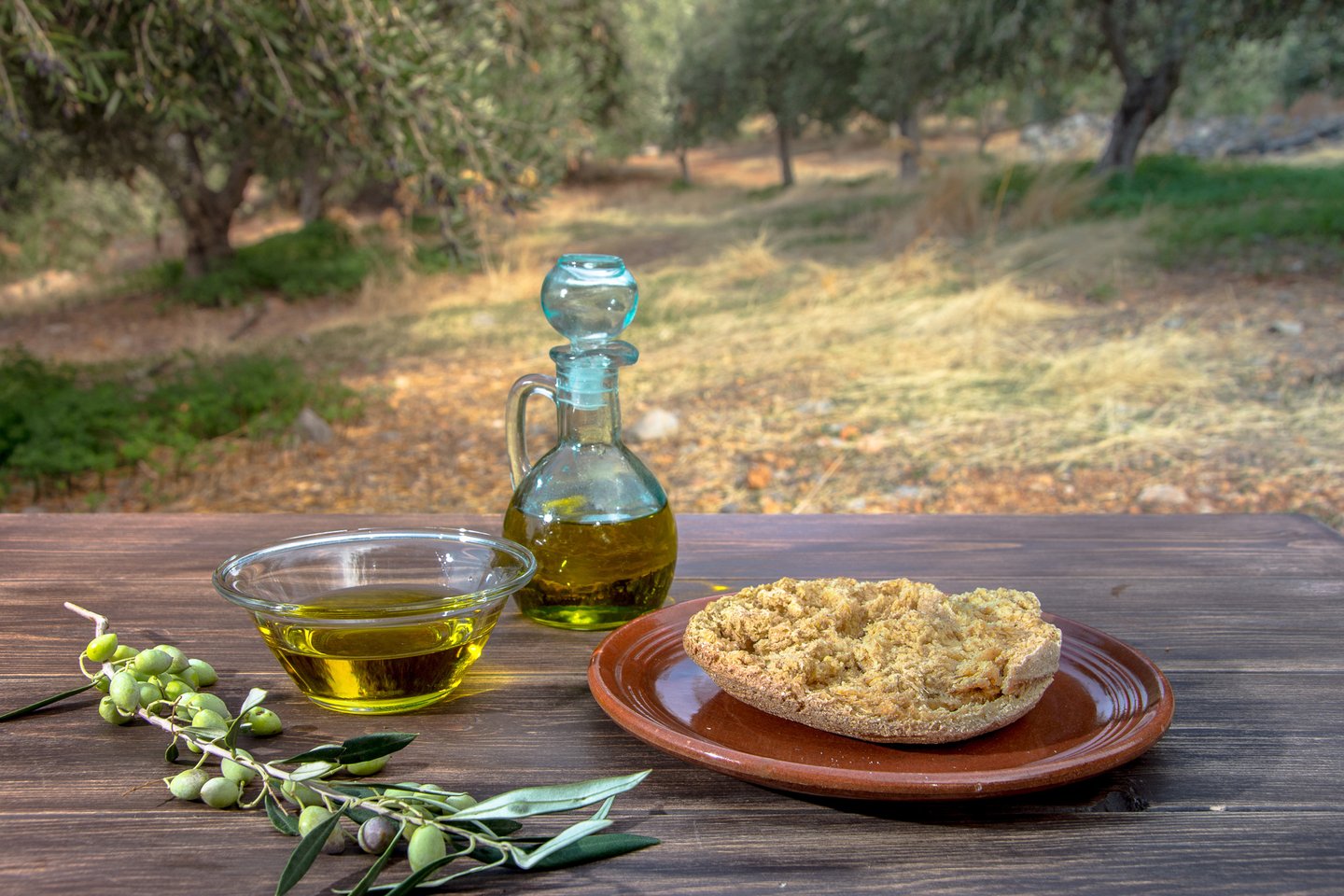 A bottle and bowl of olive oil with dakos in a Cretan olive grove